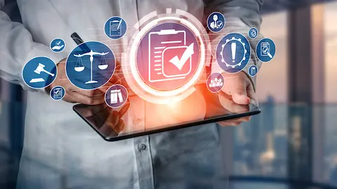 Um close-up de mãos segurando um tablet com ícones de conformidade regulatória flutuando acima dele, incluindo um documento de lista de verificação com uma marca de seleção.